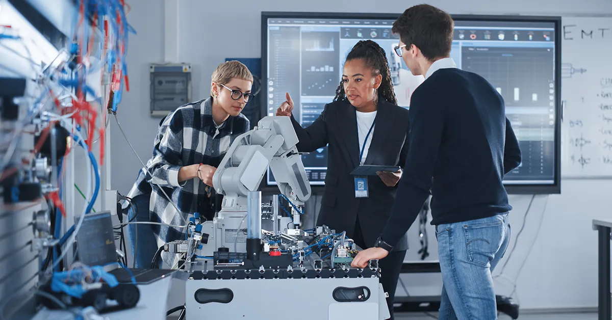 A Black female leader and two students in a robotics lab working on a robotic hand. Find out how AI is helping with accessibility at the GROW blog.